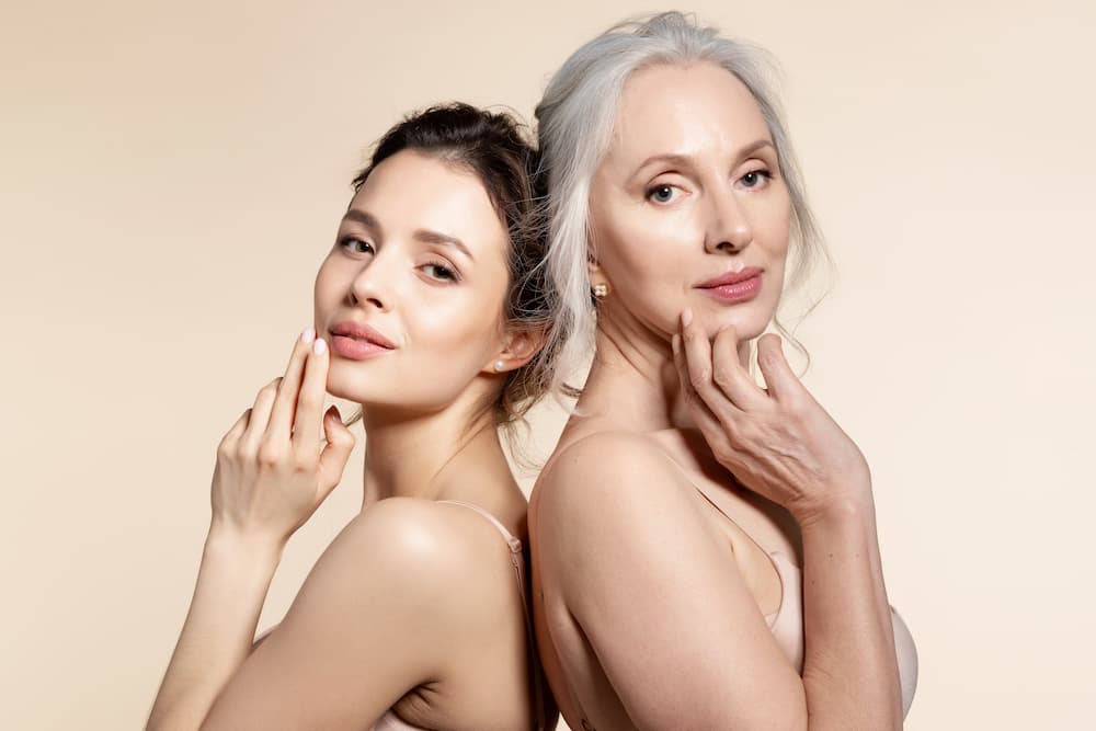 Two women of different ages standing back-to-back with healthy, radiant skin, symbolizing confidence and wellness at every stage of aging.”