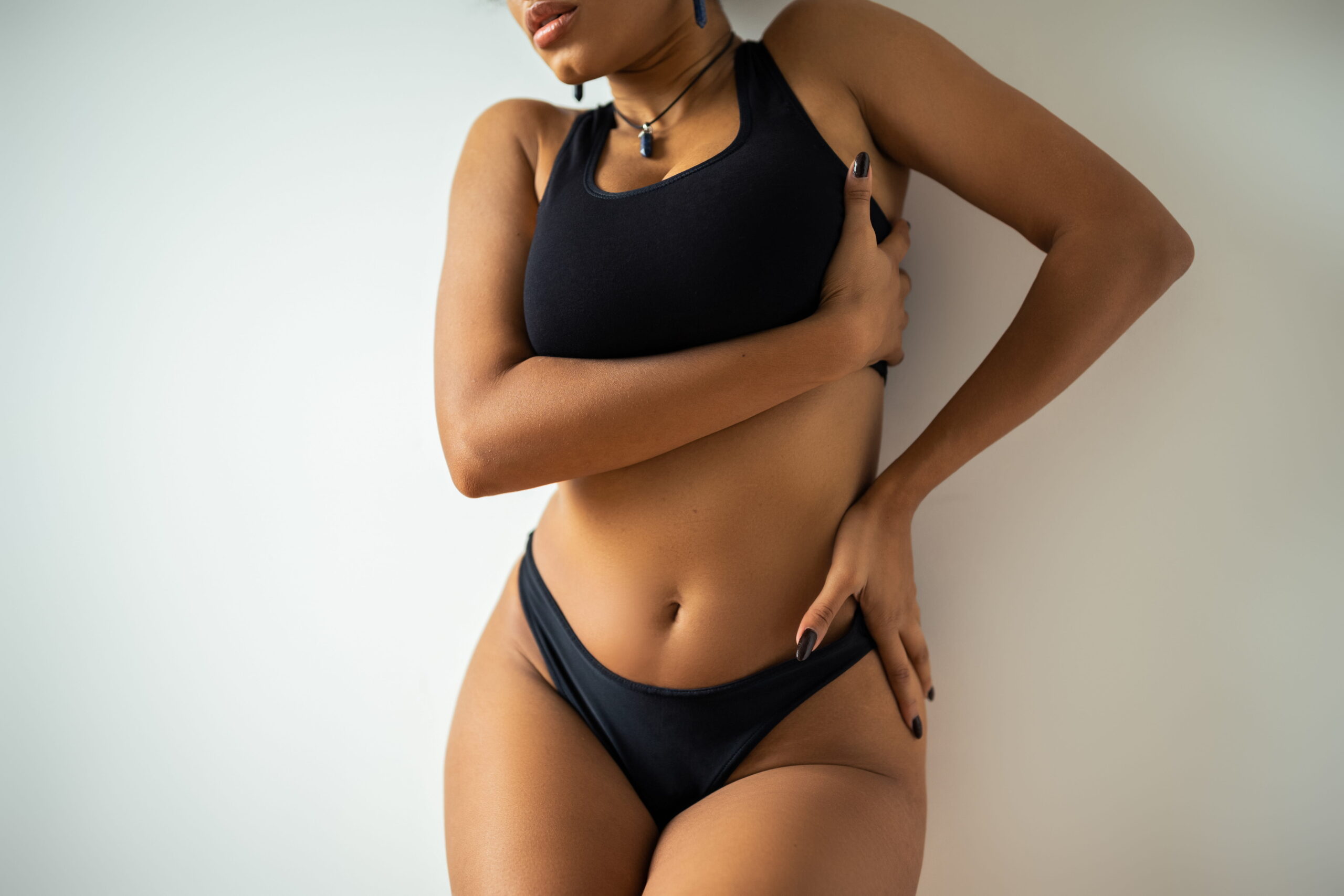 "Confident woman with toned abdomen and smooth skin posing in black athletic wear, showcasing long-lasting results from non-surgical body contouring treatment.