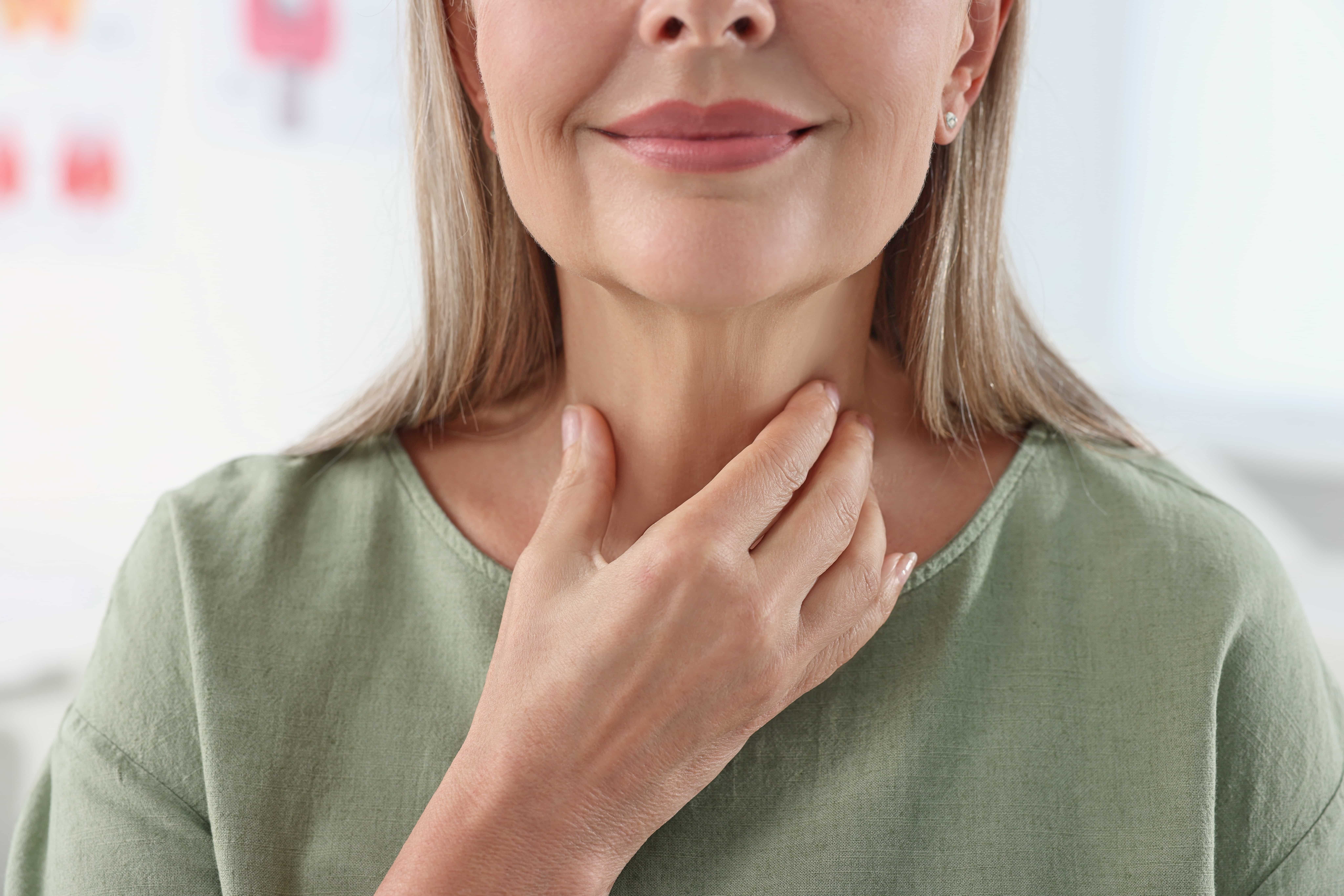 Middle-aged woman with light hair gently touching her neck to self-check thyroid gland for swelling or hormone imbalance symptoms.
