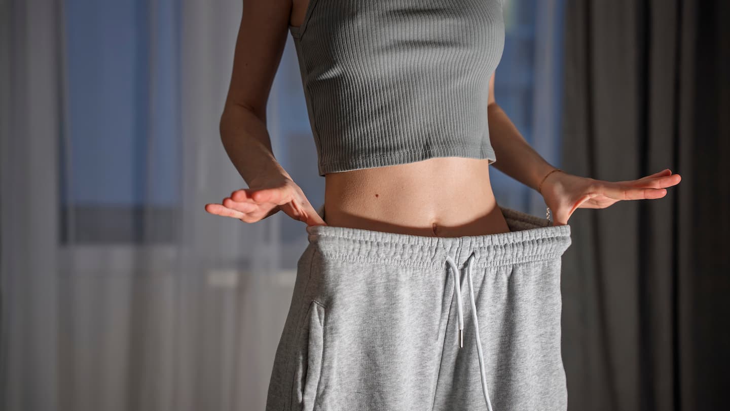 Woman showing weight loss transformation results wearing oversized pants