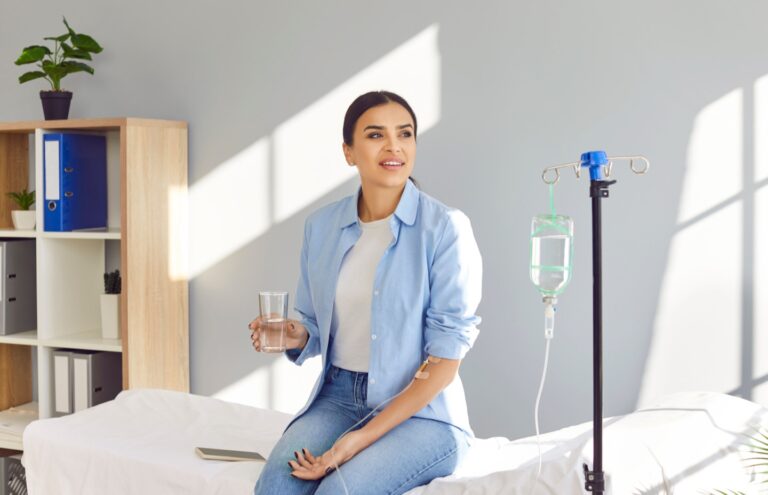Woman receiving vitamin IV hydration therapy while drinking water at a wellness clinic